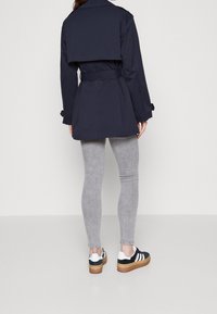 Granatowa wodoodporna kurtka z paskiem w talii, zakładanym tyłem i długimi rękawami; zestawiona z jasnoszarymi legginsami i czarnymi trampkami z białymi akcentami.