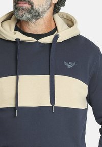 Sudadera de algodón en tonos azul marino y beige, con una gran franja beige, cordones ajustables y un pequeño logo en el pecho. Textura suave.