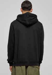 Sudadera con capucha negra de textura suave; cuenta con un bolsillo tipo canguro y puños de canalé; se lleva con pantalones cargo color verde oliva.