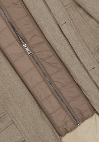 Brązowy płaszcz z mieszanki wełny z gładką pikowaną podszewką. Posiada centralny zamek błyskawiczny oraz kieszenie po bokach. Ma miękką i ciepłą fakturę.