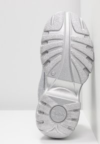 Srebrna podeszwa buta z teksturowanej gumy dla lepszej przyczepności. Charakteryzuje się delikatnym połyskiem i wyraźnym wzorem bieżnika, co poprawia przyczepność i trwałość.