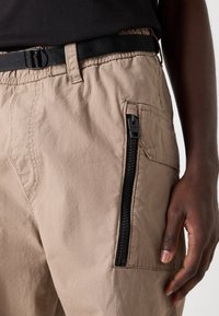 Khaki cargo trousers made of lightweight fabric, featuring a side zip pocket, elastic waistband, and a black adjustable belt.