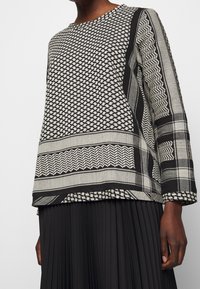 Schwarz-weißer gemusterter Langarmoberteil mit geometrischen und gestreiften Designs, kombiniert mit einem schwarzen Faltenrock.