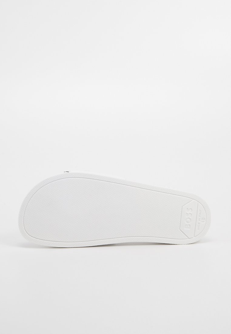 Semelle de sneaker blanche avec surface en caoutchouc texturé, présentant un talon rond et une légère cambrure. Le logo est visible dans un accent en forme de diamant.