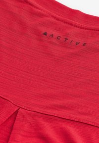 Punane aktiivne vabaaja särk, millel on pehme ja tekstureeritud kangas, ümar kaelus ning tagasi vaevu nähtav hemipool. Kaeluse taga on trükitud "ACTIVE" logo.