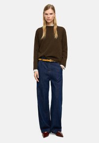 Brązowy sweter dzianinowy, szerokie niebieskie dżinsowe spodnie, żółty pasek i bordowe buty. Widoczny kołnierz w paski. Minimalistyczny design.
