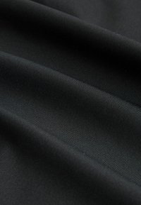 Crna tkanina s glatkom teksturom i suptilnim rebrastim uzorkom, prikazujući meke nabore i draperije, naglašavajući svoj fleksibilan, fluidan dizajn.