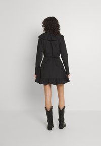 Vestido negro con dobladillo en volantes y lazo en la parte posterior, con un gran cuello. Combinado con botas de vaquero negras hasta la rodilla, de textura suave en general.