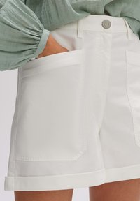 Shorts bianchi in cotone con orlo arrotolato e ampie tasche anteriori. Presentano una chiusura con bottone e una finitura liscia e tessurizzata.