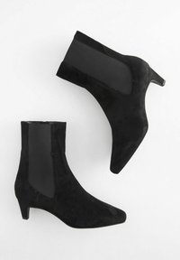 Juodos aulinukės su smailiu nosiu ir bloko kulnu. Pagamintos iš zomšos, su elastingais šoniniais įdėklais, kad būtų lengva apsiauti. Glotni tekstūra, elegantiškas dizainas.