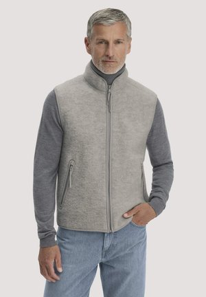 Middle-aged man wearing a light gray zip-up fleece vest over a gray long-sleeve shirt and light blue jeans, standing with one hand in pocket.