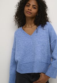 Lichtblauwe gebreide trui met een V-hals, geribde mouwen en zoom. Heeft een losse pasvorm en textuurstof, gecombineerd met donkere jeans.