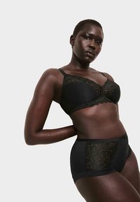 Zwarte kanten bralette met gestippeld patroon en verstelbare bandjes, gecombineerd met een bijpassend slipje met hoge taille en kanten accenten.