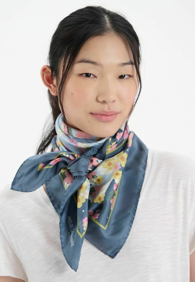 Foulard en soie avec un fond bleu et des motifs floraux en rose et jaune, noué à l'avant pour une forme structurée.