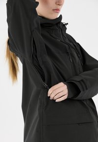 Schwarze wasserdichte Jacke mit einer taillierten Passform, mit Reißverschlüssen an den Seiten und Ärmeln sowie einem hohen Kragen zum Schutz vor den Elementen.