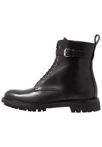 Botín negro de cuero con un acabado suave, ojaletes de metal para los cordones, correa de contraste con detalle de hebilla y una suela de goma resistente.