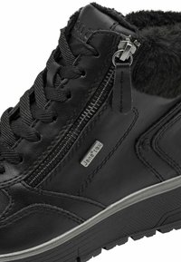 Schwarzer Lederstiefel bis zur Knöchel mit strukturiertem Fellfutter, ausgestattet mit Schnürsenkeln und seitlichem Reißverschluss. Gummisohle mit markantem Profil.