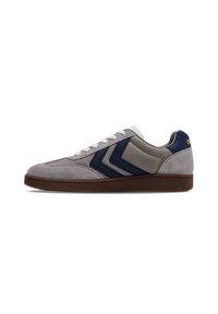 Grijze suède sneakers met marineblauwe accenten, voorzien van een getextureerd paneel en zigzagstrepen. Witte veters, een laag profiel en een bruine zool.