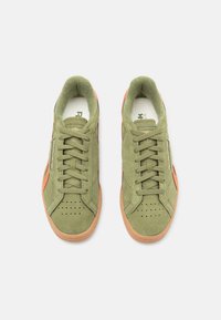 Ελαιόχρωμα σουέτ αθλητικά παπούτσια με πορτοκαλί λεπτομέρειες, υφασμάτινη επιφάνεια, επίπεδες κορδόνες, τρυπητό μπροστινό μέρος και σόλα από καουτσούκ τύπου γκάμ. 