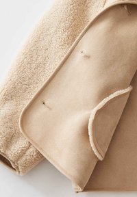 Beige Fleecejacke mit weichem, strukturiertem Außenmaterial und glattem Futter. Verfügt über verdeckte Druckknöpfe zum Schließen und ein minimalistisches Design.