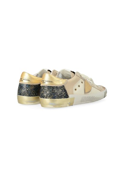 Une paire de baskets basses beiges et dorées avec des panneaux de talon en paillettes noires et des lacets blancs, inclinées pour montrer les côtés extérieurs et les talons.