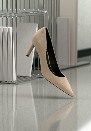 Chaussure à talon haut en daim beige flottant au-dessus d'une surface réfléchissante avec des organiseurs de dossiers en métal et des documents en arrière-plan.