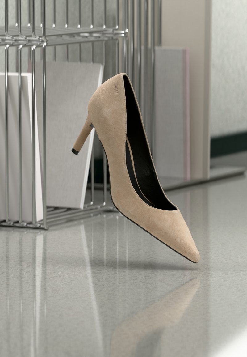 Chaussure à talon haut en daim beige flottant au-dessus d'une surface réfléchissante avec des organiseurs de dossiers en métal et des documents en arrière-plan.