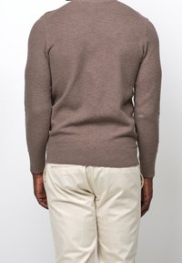 Brauner, gestrickter Pullover mit langen Ärmeln, gerippten Bündchen und Saum, kombiniert mit hellbeigen Hosen. Einfaches, strukturiertes Design, keine sichtbaren Muster.