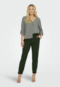 Blusa gris claro con lunares texturizados, con botones en el frente y mangas enrolladas, combinada con pantalones verdes a medida y sandalias nude.