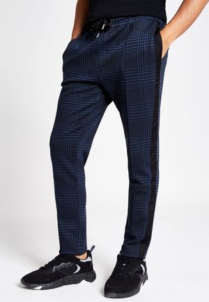 Pantaloni jogger a quadri blu navy con vestibilità rilassata, cintura elastica, tasche laterali e strisce nere laterali, abbinati a sneakers nere.