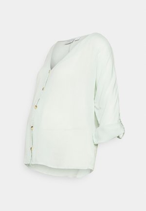Blouse vert clair à boutons, en tissu doux, avec un col en V, des manches retroussables et une coupe décontractée avec un ourlet arrondi.