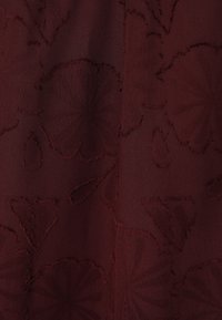 Ciemnobordowy materiał o fakturze z kwiatowym i kroplowym wzorem, z wypukłymi, przeszywanymi konturami i różnorodnymi splotami tkaniny.