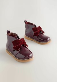 G glänzende bordeauxroten Lackleder-Stiefeletten mit einer großen Samtschleife, Gummisohle und kariertem Innenfutter. Mit einem Schlaufenabsatz für einfaches Anziehen.