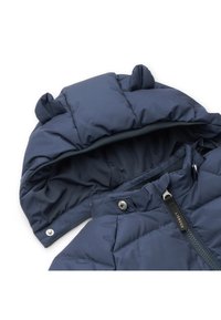 Tumedast sinine polsterdatud jope kapuutsiga, millel on karu kõrvad, lukuga ja nööbiga kinnitamine. Sile, tikandiga tekstuur, ideaalne soojuse tagamiseks.