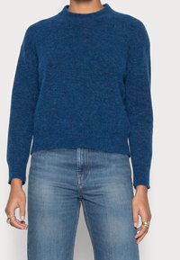 Pull court bleu avec un col rond, des manches longues et un tricot doux et texturé. Associé à un jean bleu clair.