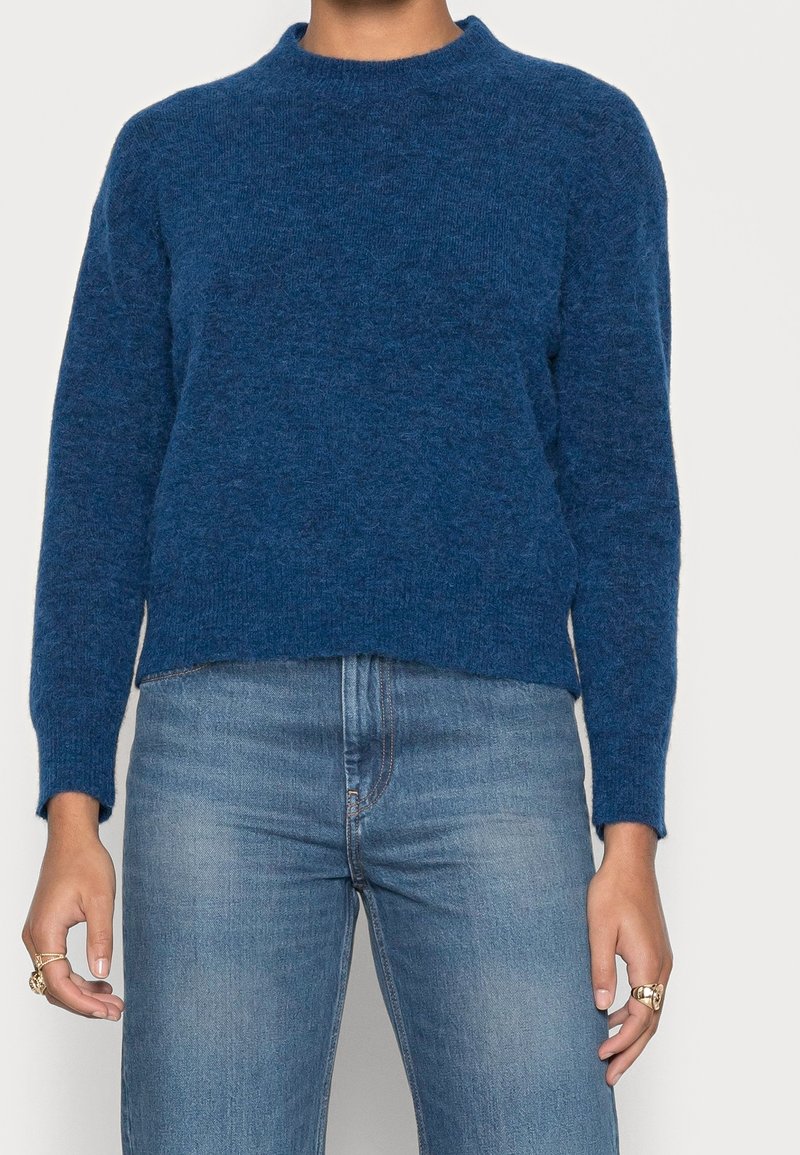 Pull court bleu avec un col rond, des manches longues et un tricot doux et texturé. Associé à un jean bleu clair.