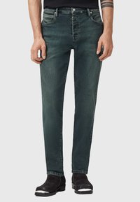 Tmavě modré džínsy slim fit s pěti kapsami, vybledlým vzhledem a jemnými šmouhami. Zapínání na kovový knoflík a zip.