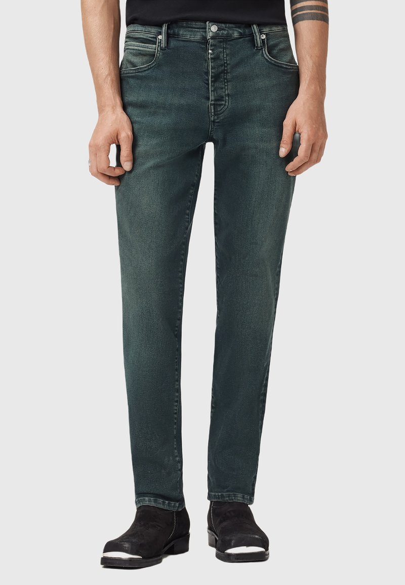 Tmavě modré džínsy slim fit s pěti kapsami, vybledlým vzhledem a jemnými šmouhami. Zapínání na kovový knoflík a zip.