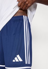 Marineblaue Sportshorts mit weißen Streifen, elastischem Bund und Logo unten links. Das Material ist glatt und leicht, ideal für aktive Freizeitkleidung.
