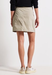 Beige katoenen rok met een uitlopende vorm, zichtbare stikdetails en een rechte zoom. Gecombineerd met witte en beige sneakers.