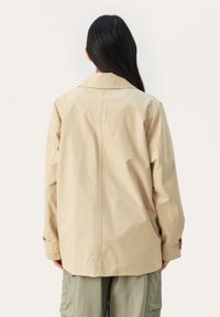Beige bomuldsjakke med krave, afslappet pasform og lange ærmer, med en bagsøm og manchet-detaljer.