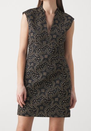 Robe noire sans manches avec motifs d'étoiles dorées en forme de clous, décolleté en V profond, portée par une personne debout sur un fond clair uni.