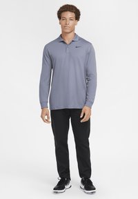 Long-sleeve gray polo shirt with a collar, Nike logo on the left chest, paired with black pants and black athletic shoes.