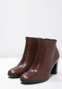 Ruske nahodne kožne čizme sa zatvaračem, zakrivljenog oblika, teksturiranim obrubom na vrhu i blok petom. Glatka završna obrada i minimalni detalji.