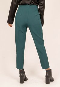 Pantalons taille haute teal en tissu lisse, avec une coupe ajustée et des jambes fuselées, associés à des bottines à talons noires.