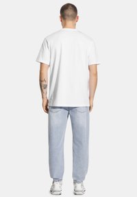 Biała bawełniana koszulka z krótkim rękawem, luźny krój, połączona z jasnoniebieskimi dżinsami i białymi trampkami. Widok z tyłu pokazuje proste detale szycia.