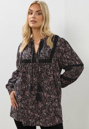 Blusa nera con motivi floreali in rosa e bianco, con uno yoke nero in tessuto testurizzato, lacci con pon pon e lunghe maniche a sbuffo.