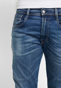 Jeans din denim de un albastru deschis, cu un design clasic cu cinci buzunare, ușor decolorate și detalii ale cusăturilor contrastante. Închidere cu buton și fermoar.
