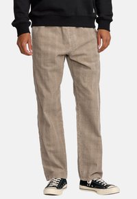 Beige geruite relaxte broek met een gestructureerde afwerking, voorzien van een rechte pijp en gedragen met zwarte canvas sneakers.