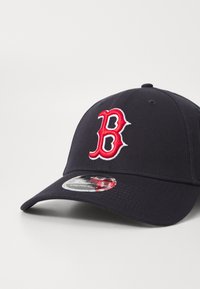 Gorra de béisbol marina hecha de tela con un logotipo bordado en rojo de la "B". Presenta un pico curvado y un cierre trasero ajustable.